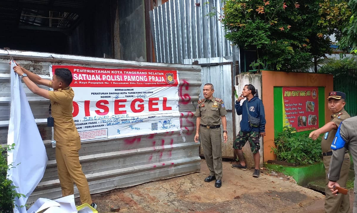 Satpol PP Kota Tangerang Selatan membuka segel yang ditutup kain pada pembangunan pabrik masker di Pondok Aren